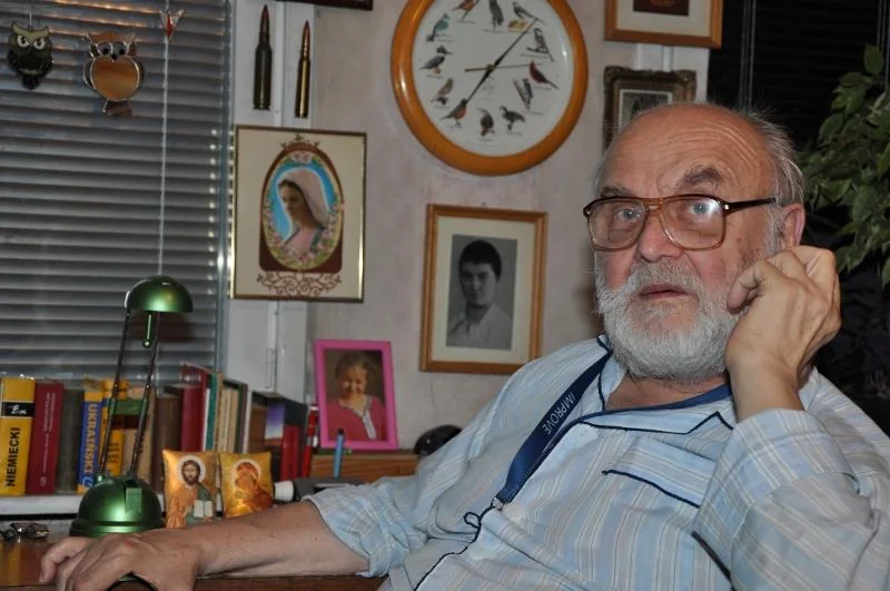 Andrzej Lech Ruprecht seated in his study, surrounded by books, photographs, and a bird clock